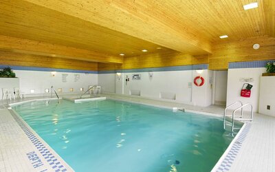 The hotel’s indoor pool is brightly lit and has chairs by the side.