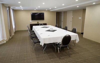 Meeting room in Les Suites Hotel Ottawa, with long table, ten chairs around it, and a large television.