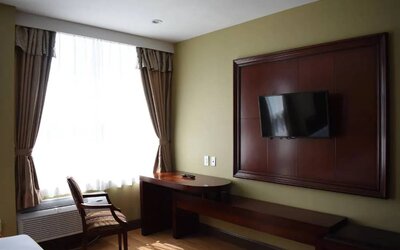 A Queens Hotel guest room with chair and table for working, and a nearby window.