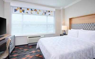 Double bed guest room in Holiday Inn & Suites Oakville At Bronte, with large window and bedside lamp.