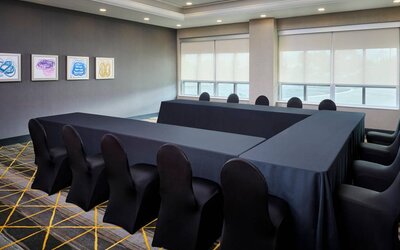 Hotel meeting room with three tables arranged in a U-shape and seating for over a dozen attendees.