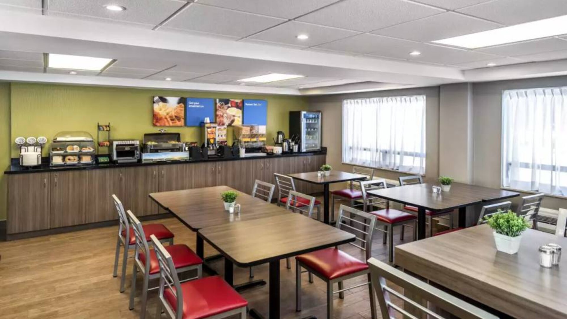 The hotel breakfast area has a hard floor, large windows, and tables for four to six diners.