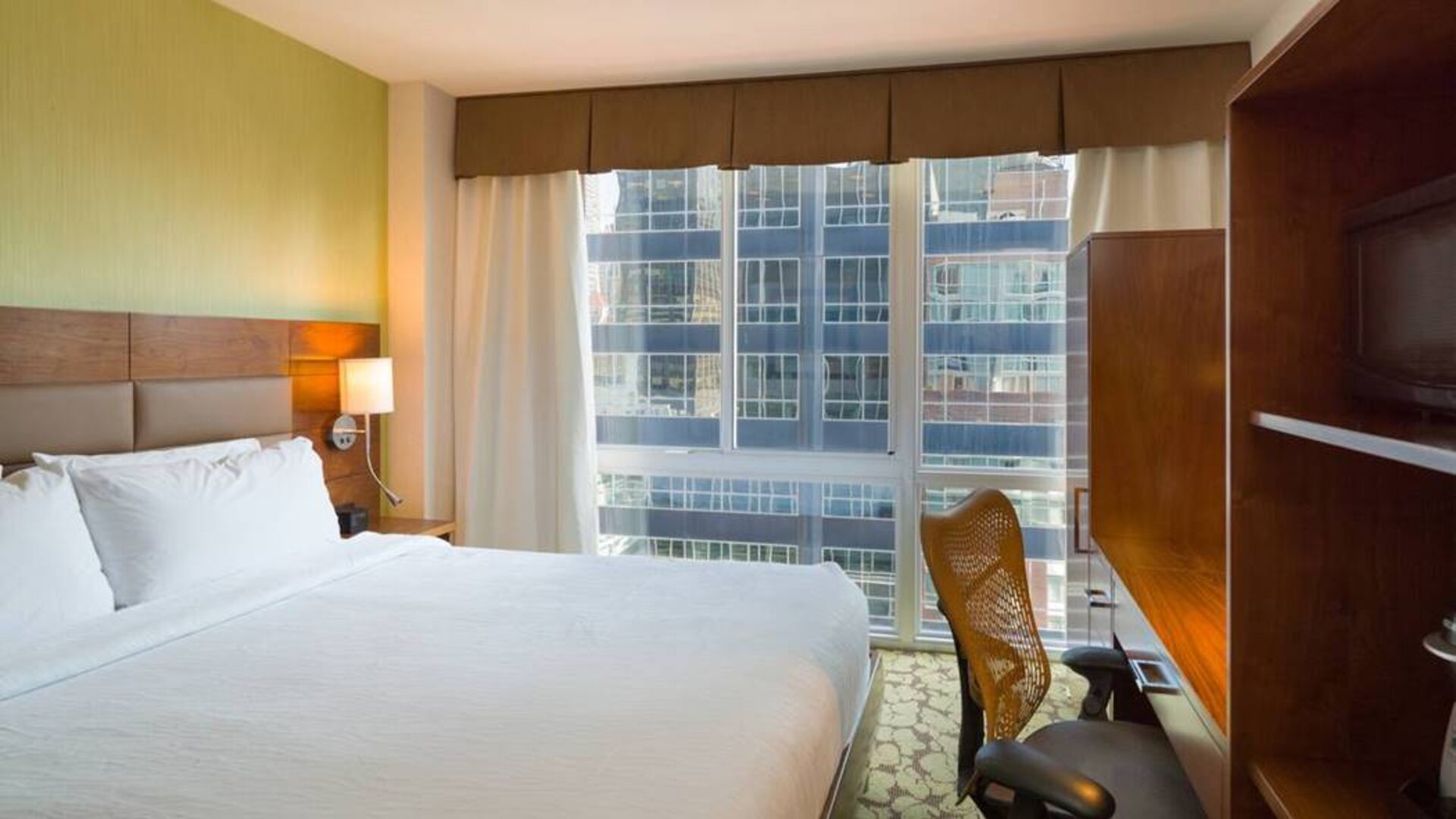 A Hilton Garden Inn Midtown East guest room with king-sized bed and floor-to-ceiling windows.