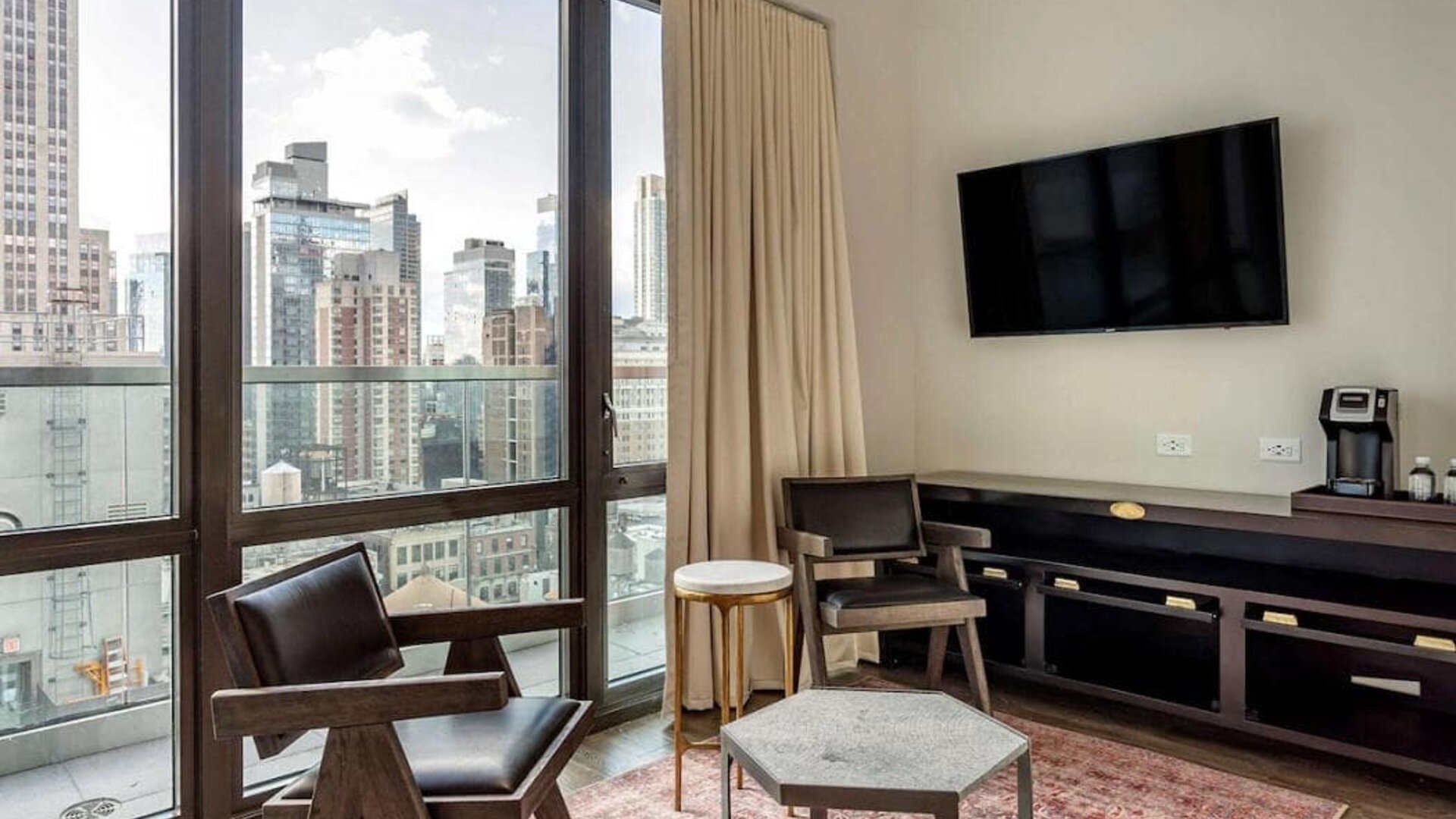Guest room in The Draper, Ascend Hotel Collection, with two chairs, coffee table, large television, and urban vista through the window.