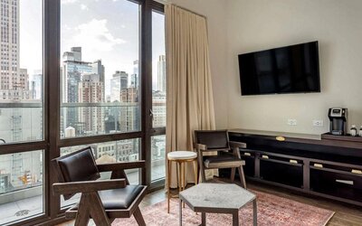Guest room in The Draper, Ascend Hotel Collection, with two chairs, coffee table, large television, and urban vista through the window.