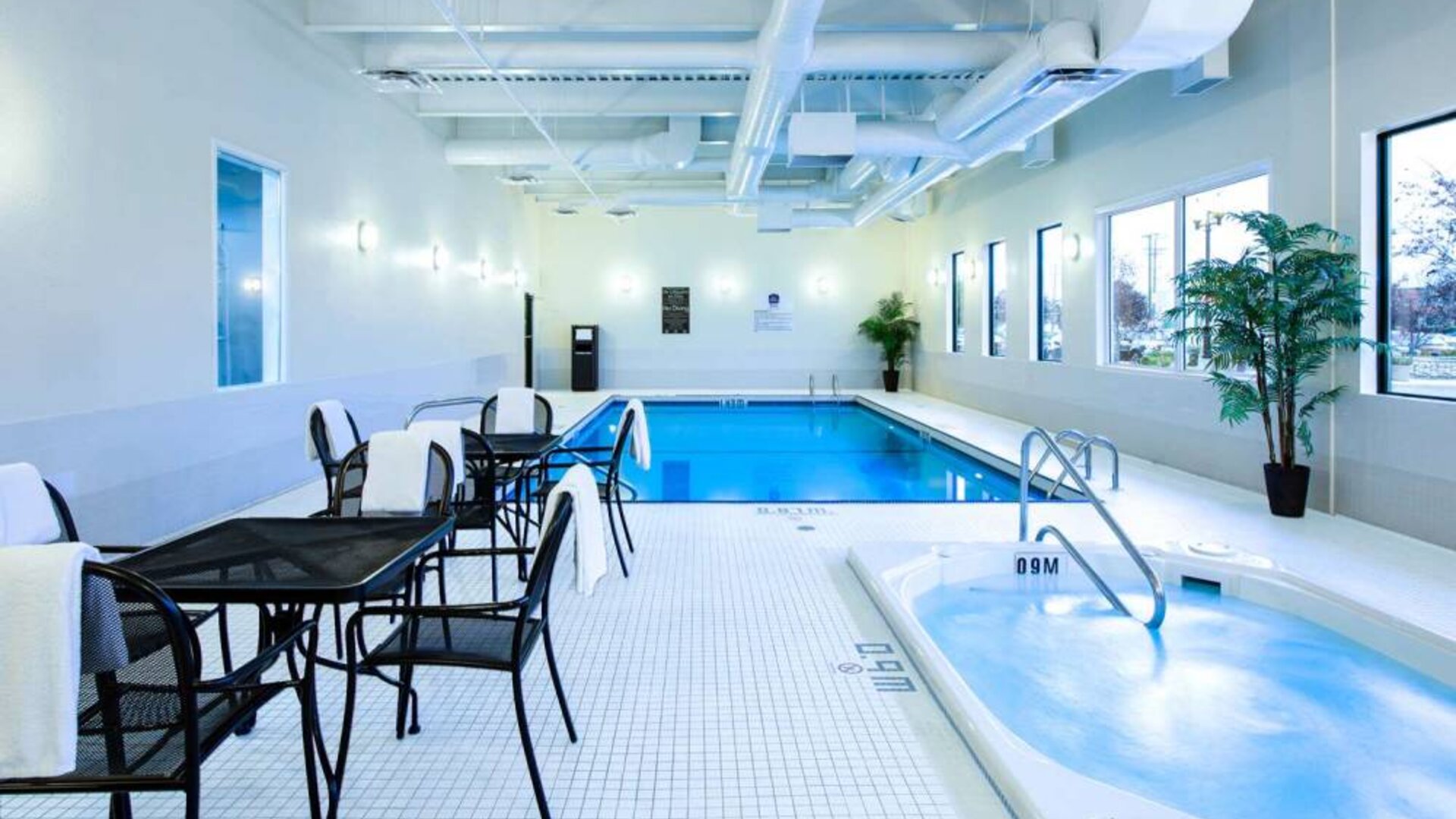 The hotel’s indoor swimming pool has tables, chairs, potted plants, and a hot tub nearby.