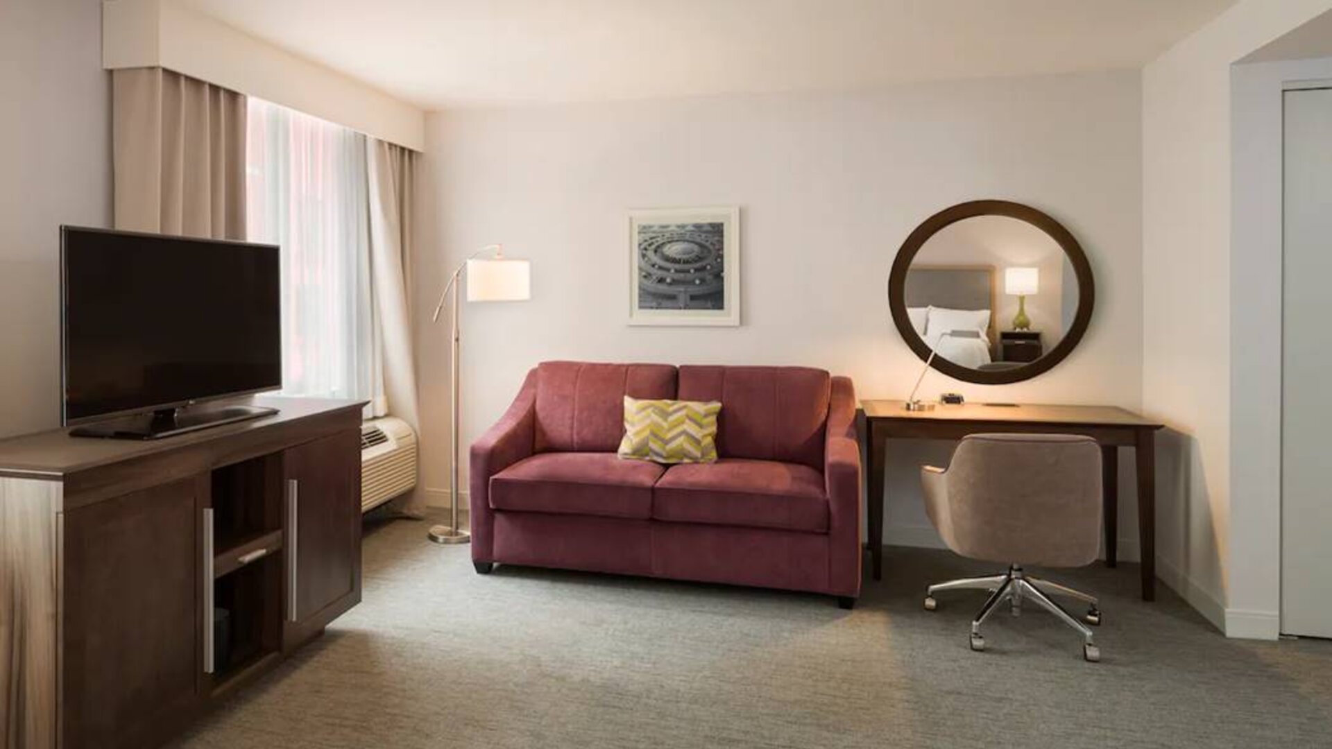 The Hampton Inn Times Square South’s king mobility suite lounge, with desk, sofa, and television.