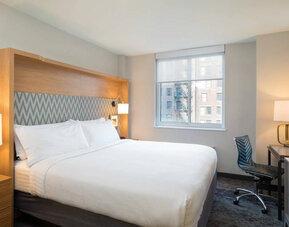One of Holiday Inn Express Wall Street’s guest rooms, complete with double bed, window, and workspace chair and desk.