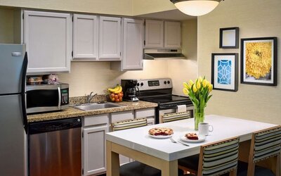 Sonesta ES Suites Tucson guest room kitchen area, equipped with hob, oven, microwave, sink, and fridge freezer, plus dining table.