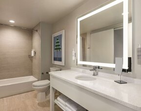 Private guest bathroom with tub and free toiletries at Embassy Suites By Hilton Panama City Beach Resort.