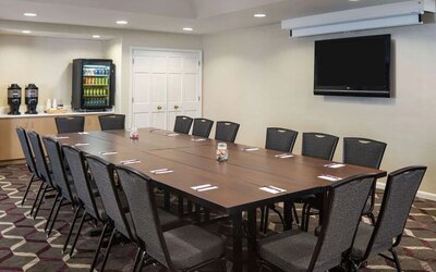 Hotel meeting room, including a long wooden table, projector screen, wall-mounted TV, and seating for over a dozen attendees.