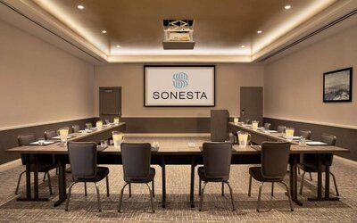 Hotel meeting room with long tables arranged in a U-shape, facing a large projector screen.