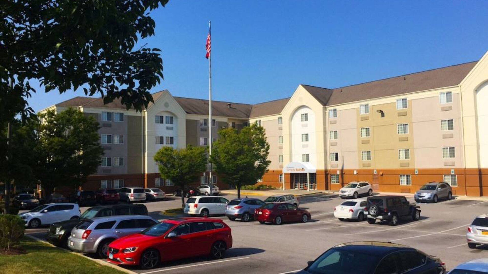 The hotel exterior features ample parking, pleasant greenery, and a fluttering Stars and Stripes flag.