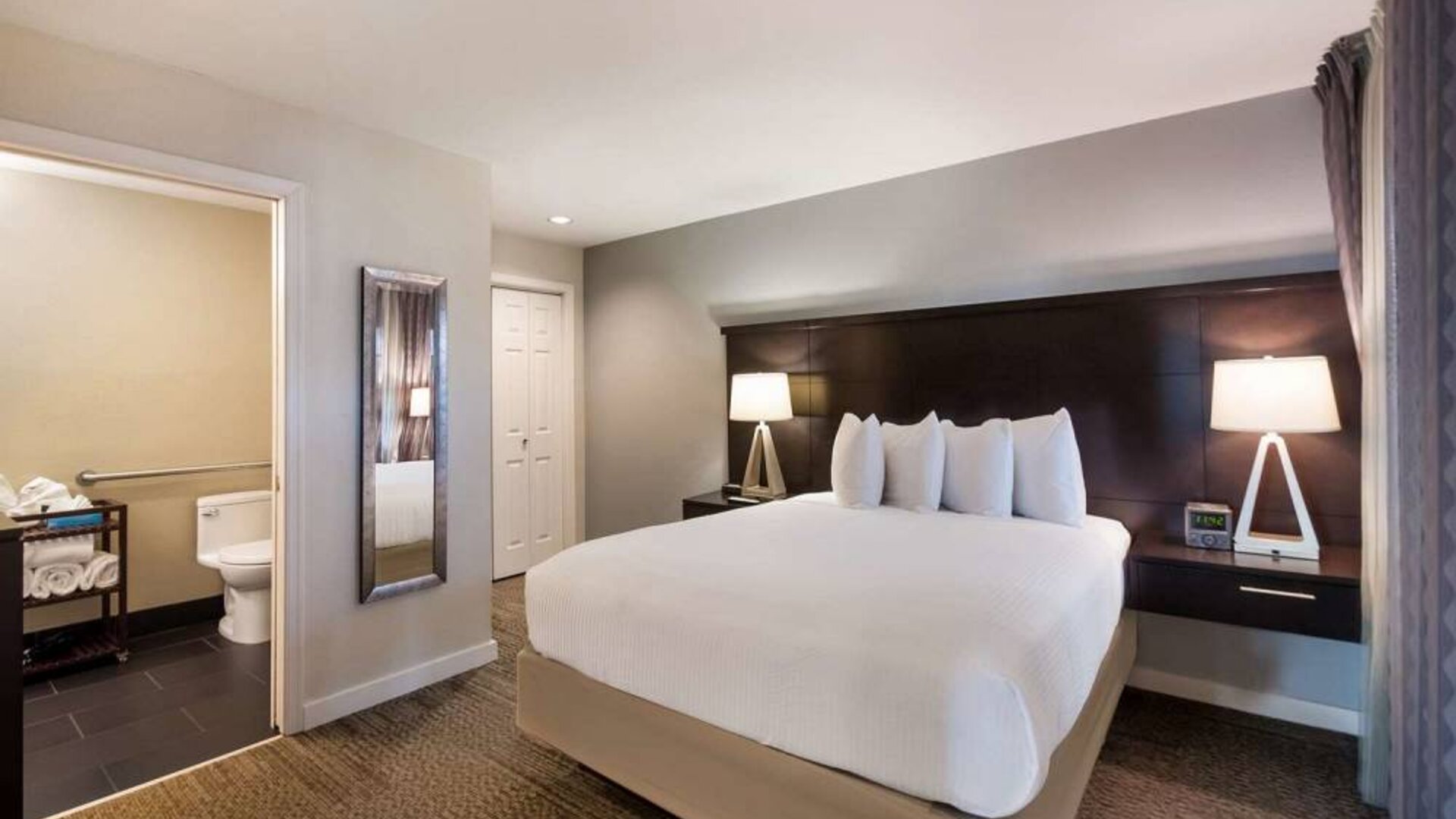 Double bed guest room in Sonesta ES Suites Dulles Airport, with tall mirror and ensuite bathroom.