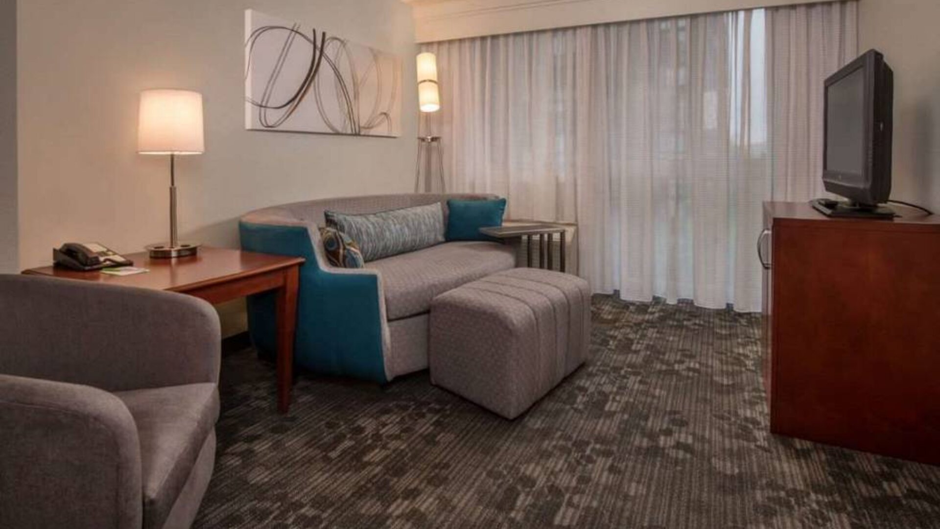 Sonesta Select Arlington Rosslyn guest room lounge with sofa, armchair, window, and TV.