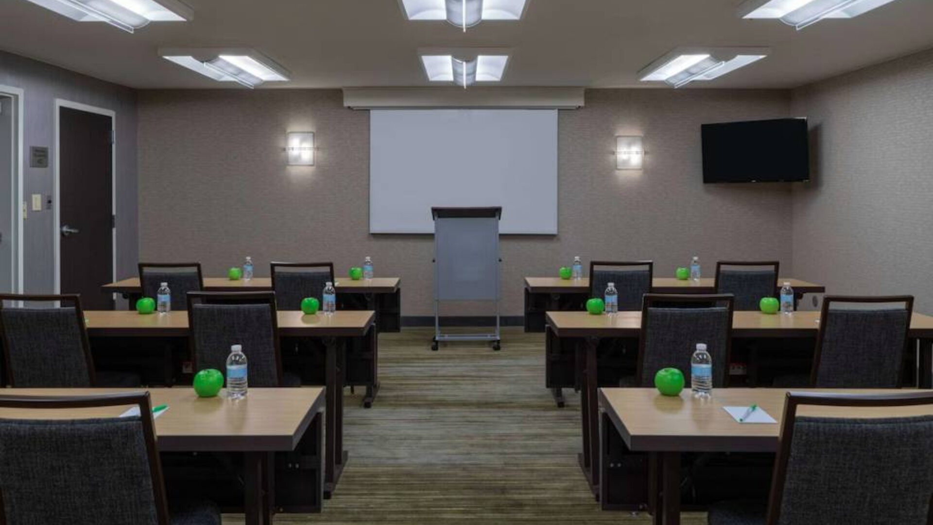 Hotel meeting room, with tables arranged in a classroom format, facing a lectern, TV, and whiteboard.