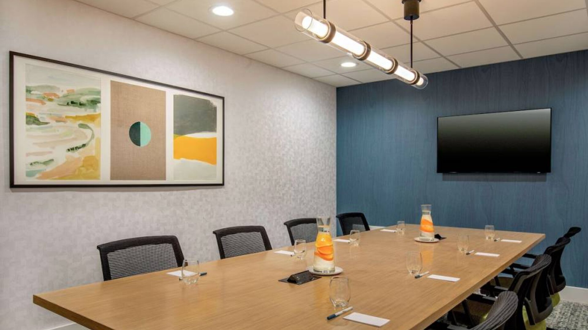 Meeting room in Sonesta Select Boston Foxborough Mansfield with long wooden table, eight chairs, and a large, wall-mounted TV.