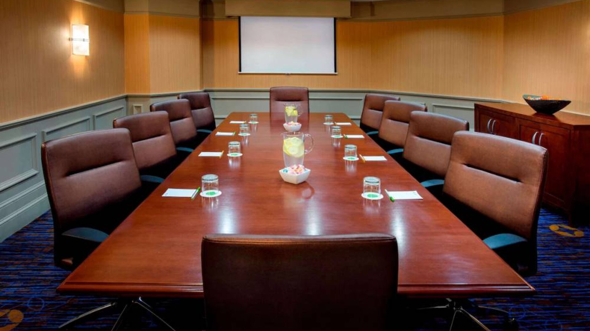 Sonesta Select Boston Danvers meeting room, with ten swivel chairs around a long table, and a projector screen.