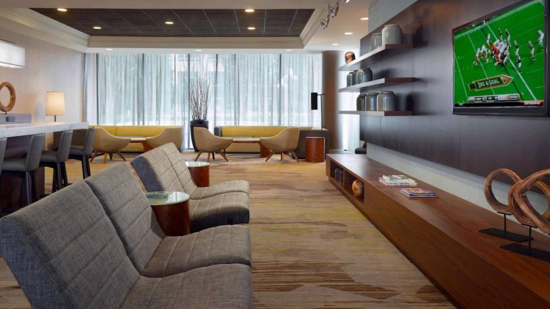Sonesta Select Atlanta Cumberland Galleria’s lobby has a large, wall-mounted TV, comfortable seating, and coffee tables.