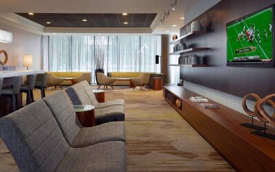 Sonesta Select Atlanta Cumberland Galleria’s lobby has a large, wall-mounted TV, comfortable seating, and coffee tables.