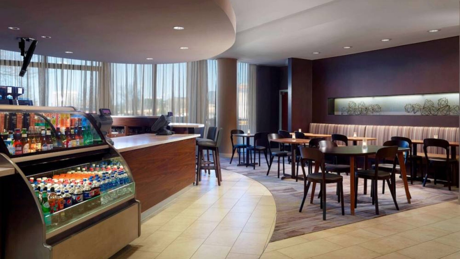 Sonesta Select Atlanta Cumberland Galleria’s dining area features a bar, both tall stool and table seating, and large windows.