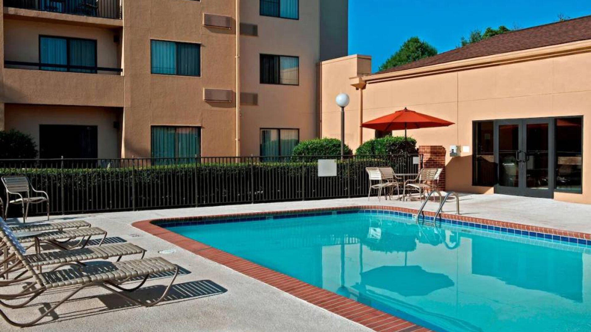 Sonesta Select Charlotte University Research Park’s outdoor pool has sun loungers and a shaded table and chairs by the side.
