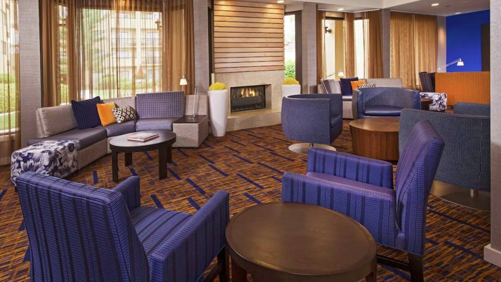 Sonesta Select Charlotte University Research Park’s lobby is furnished with a fireplace, large windows, coffee tables, and comfortable seating.