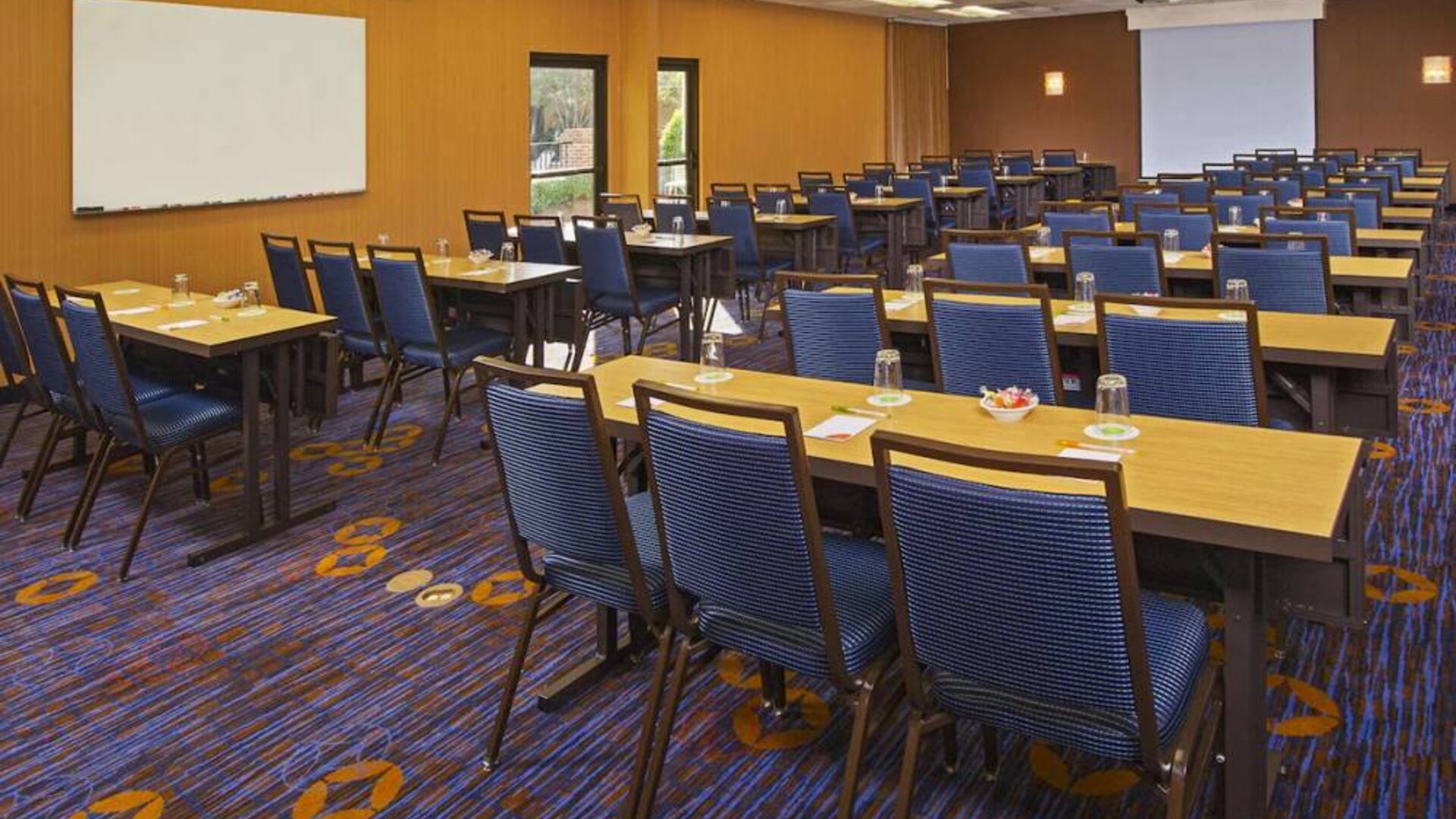 Hotel meeting room, featuring tables arranged in a classroom style facing a projector screen, with a whiteboard to one side.