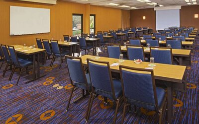 Hotel meeting room, featuring tables arranged in a classroom style facing a projector screen, with a whiteboard to one side.