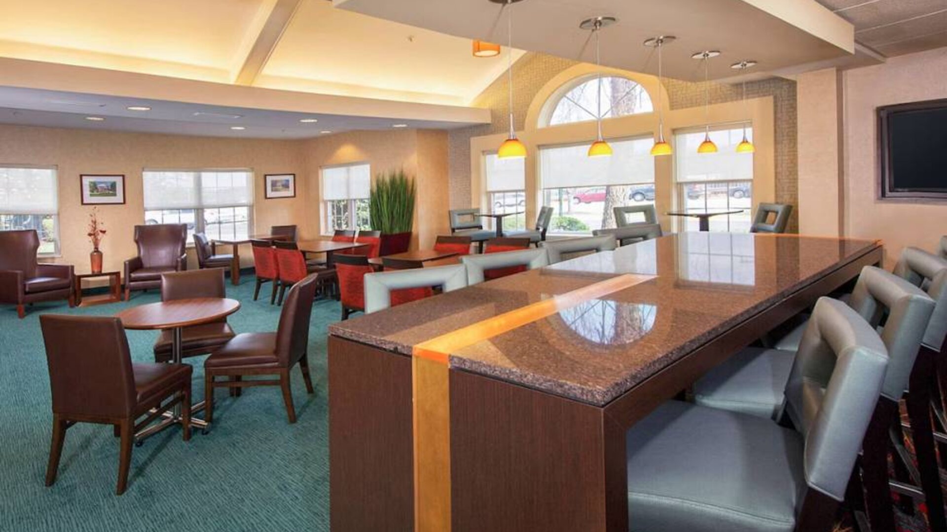 Sonesta ES Suites Charlottesville University’s lobby has extensive seating, including armchairs, table seating, and tall stools, plus a wall-mounted TV.