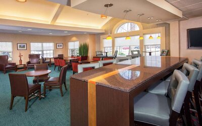 Sonesta ES Suites Charlottesville University’s lobby has extensive seating, including armchairs, table seating, and tall stools, plus a wall-mounted TV.