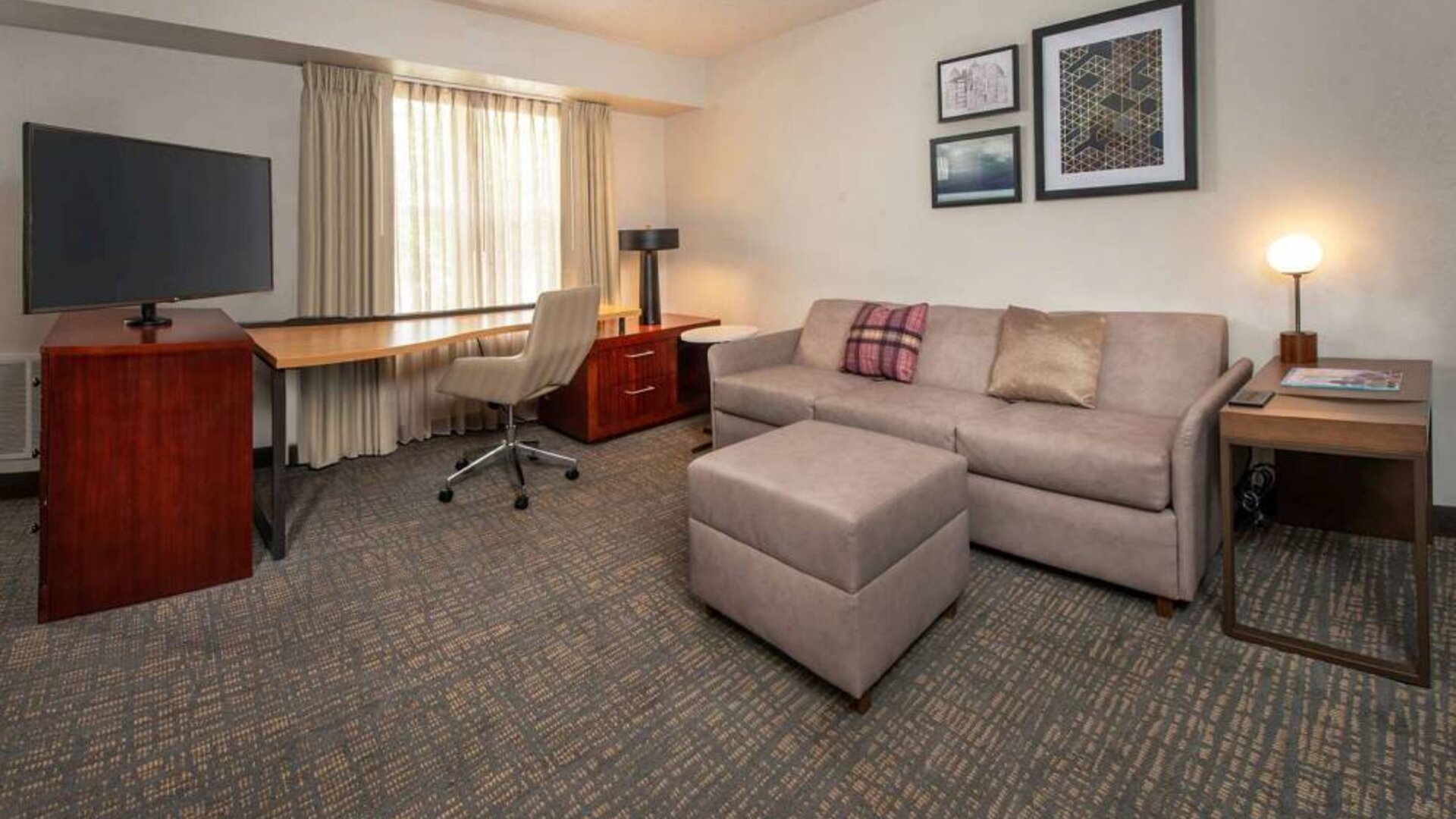 Sonesta ES Suites Baltimore BWI Airport guest room workspace, featuring chair, desk, and TV, plus a sofa nearby.