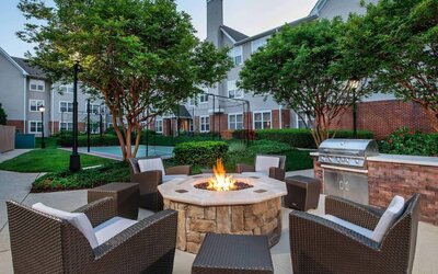 Sonesta ES Suites Baltimore BWI Airport’s fire pit is surrounded by armchairs and coffee tables, with a barbecue conveniently close.