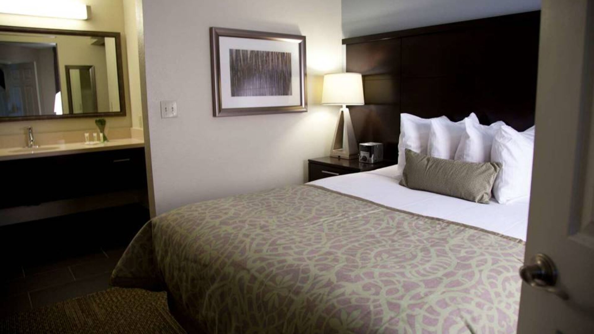 Double bed guest room in Sonesta ES Suites San Jose Airport, with bedside lamp and ensuite bathroom.