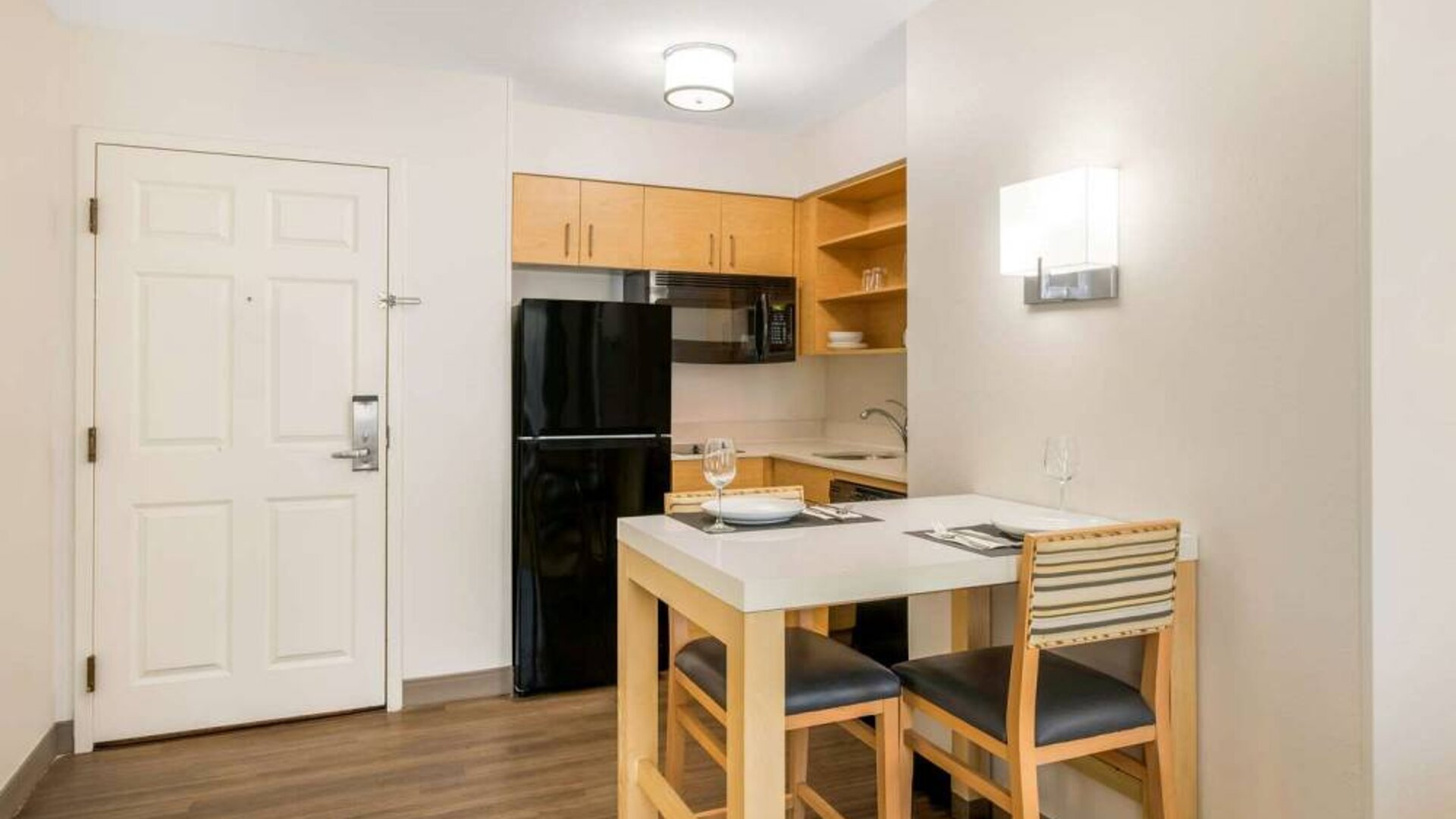 Sonesta ES Suites Charlotte Arrowood guest room kitchen area, with fridge-freezer, small table, sink, oven, and microwave.