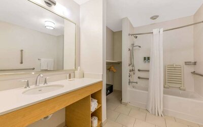 Guest bathroom in Sonesta ES Suites Charlotte Arrowood, furnished with large mirror, sink, bath and shower.