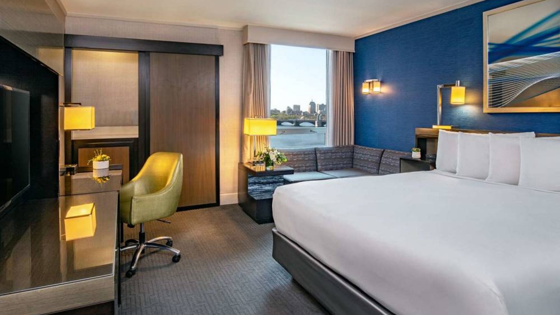 Double bed guest room in Royal Sonesta Boston, furnished with corner sofa and coffee table, comfy chair, and wall-mounted TV.