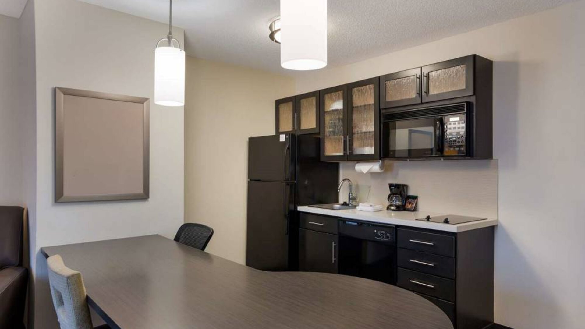 Sonesta Simply Suites Des Moines guest room kitchen, including oven, hob, microwave, fridge-freezer, and a breakfast table.