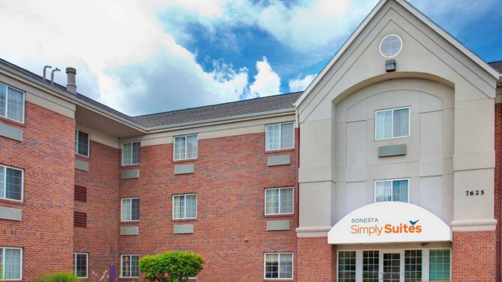 Sonesta Simply Suites Des Moines’ exterior has pleasant greenery, parking, and red brick architecture.