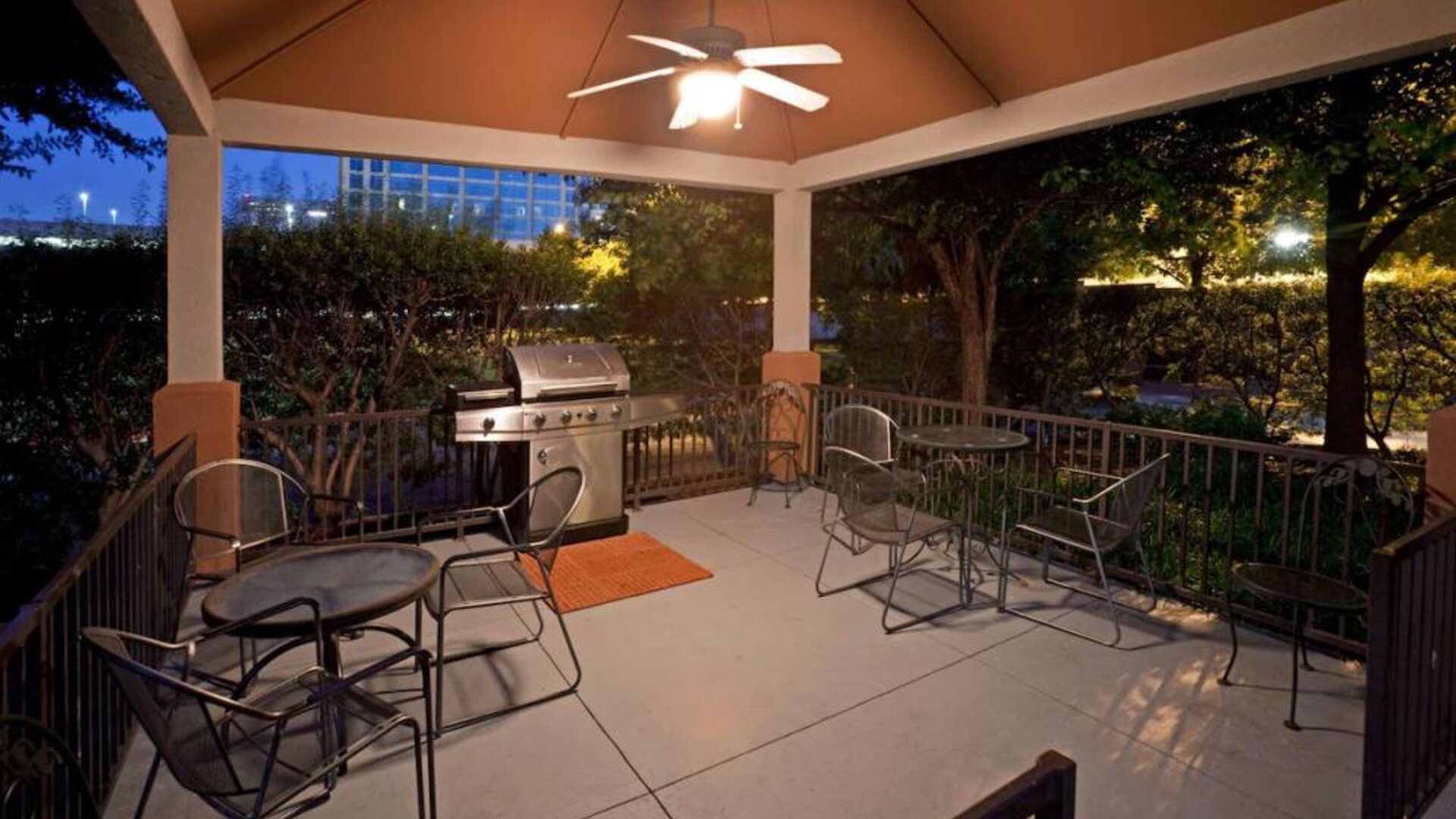 Sonesta Simply Suites Dallas Galleria’s barbecue area features tables and chairs under cover, with barbecue facilities and nearby trees.