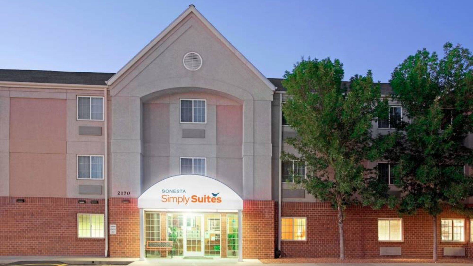 The hotel’s exterior has parking for guests on one side of the covered entrance, and trees to the other side.