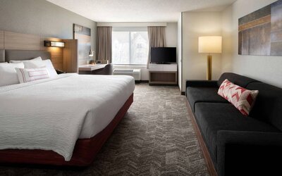 Sonesta Select Seattle Renton double bed guest room, with sofa, workspace desk and chair, TV, and large window.