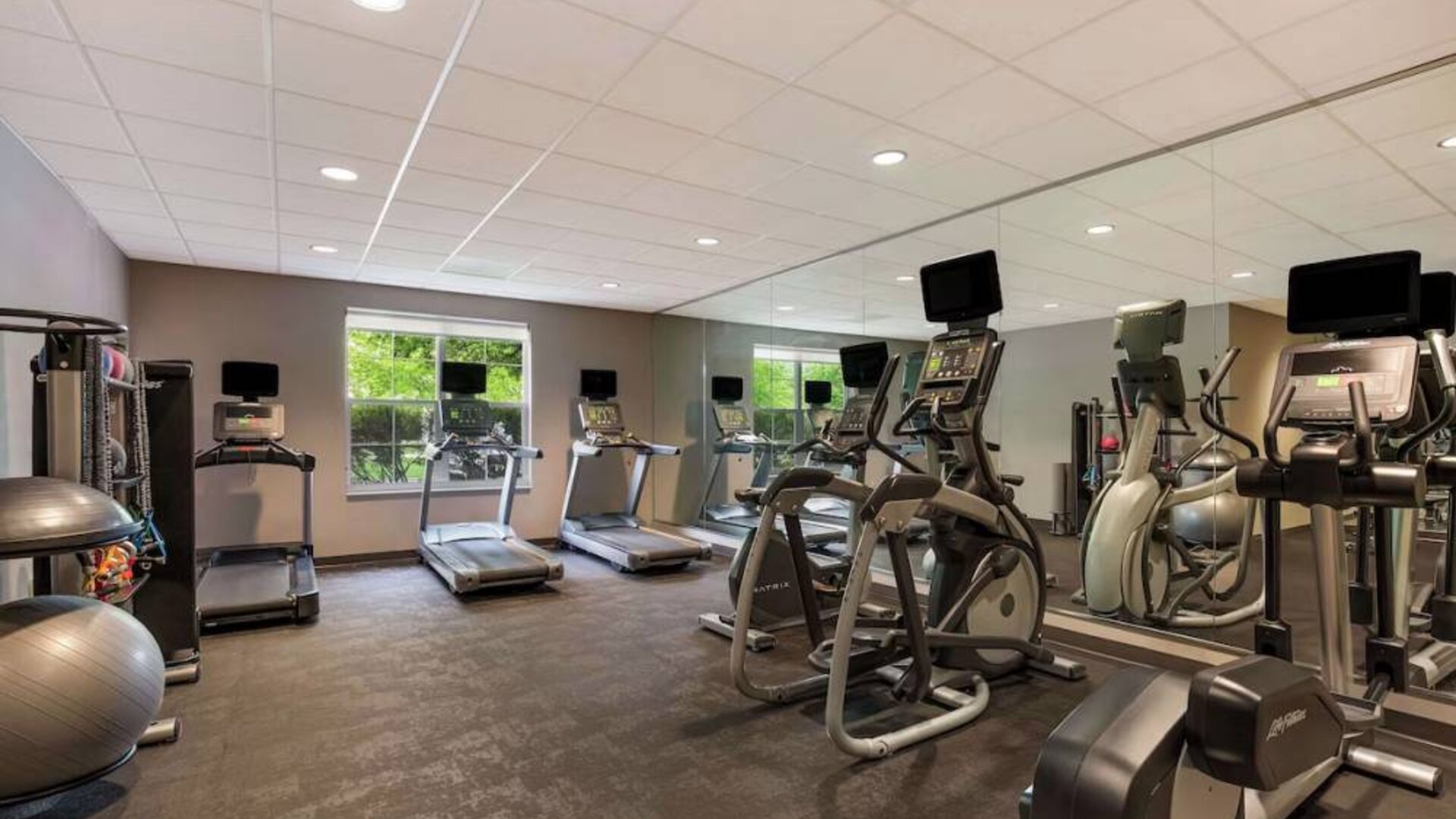 The fitness center in Sonesta ES Suites Parsippany Morris Plains has windows with green views and a wide range of exercise machines.