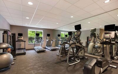 The fitness center in Sonesta ES Suites Parsippany Morris Plains has windows with green views and a wide range of exercise machines.
