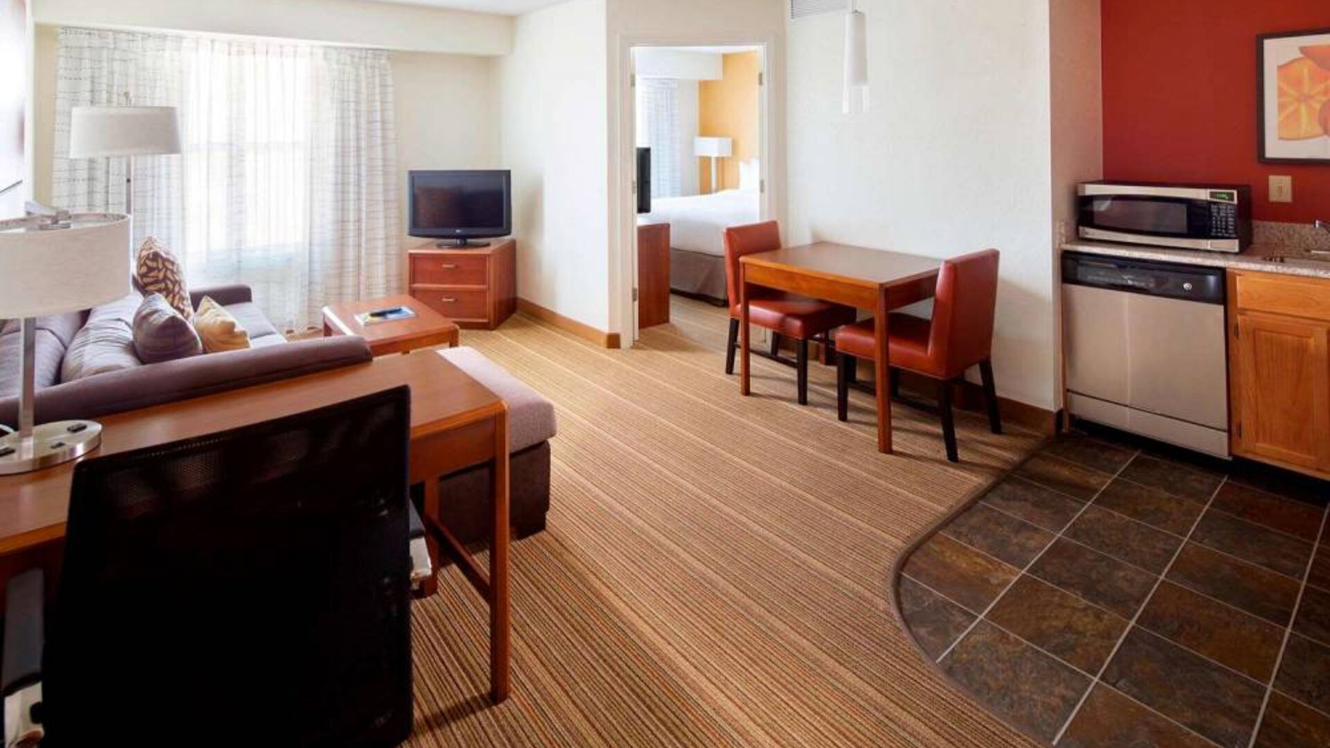 Sonesta ES Suites Birmingham Homewood double bed guest room lounge area, featuring sofa, chairs, coffee tables, window, and TV.