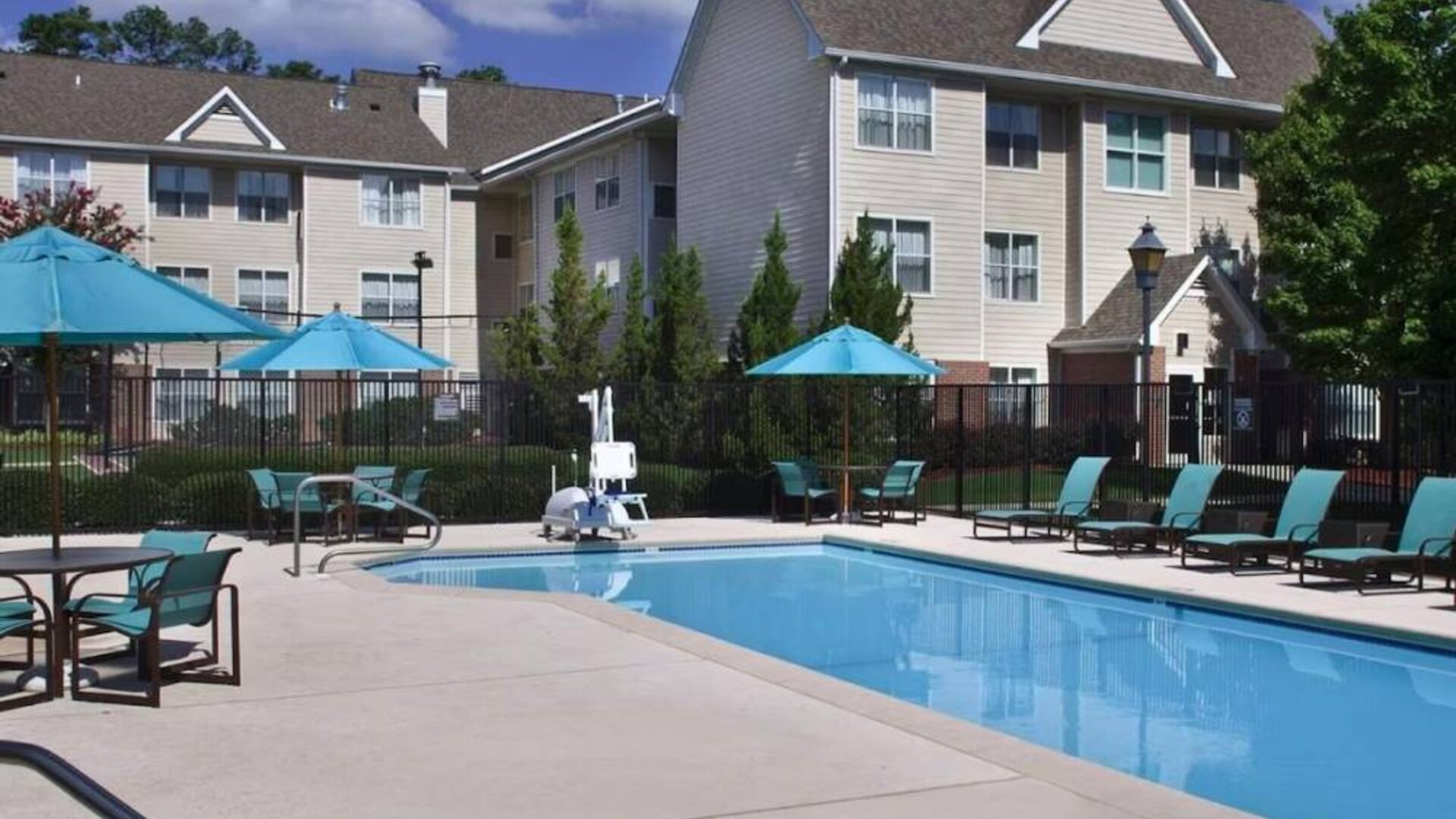 The outdoor pool of Sonesta ES Suites Birmingham Homewood is equipped with a lift, and both sun loungers and shaded tables/chairs are in the vicinity.