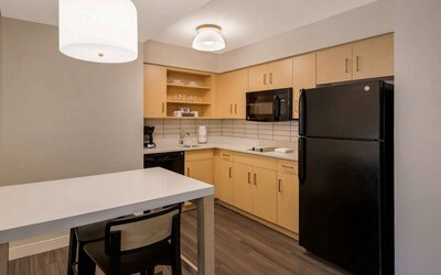 Sonesta ES Suites Andover Boston guest room kitchen, featuring oven, hob, microwave, fridge-freezer, and a kitchen table with two stools.