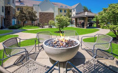 Sonesta ES Suites Andover Boston’s fire-pit is located amid pleasant greenery and surrounded by chairs, with the gazebo and barbecue facilities nearby.