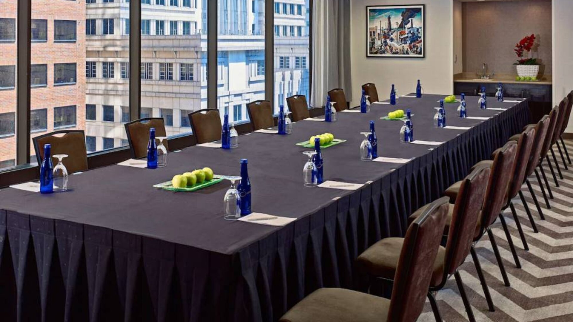 Sonesta Philadelphia Rittenhouse Square meeting room, featuring long table with space for over a dozen attendees, city views through the large windows, and art on the wall.