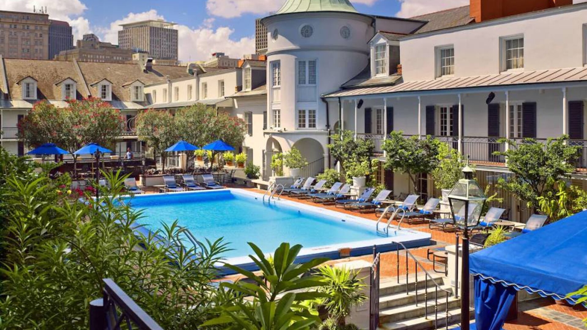 Royal Sonesta New Orleans’ outdoor pool has sun loungers by the side and shaded tables and chairs, and trees, nearby.